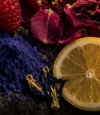 Conceptual render: butterfly pea powder and flowers, rose petals, a raspberry and a lemon slice